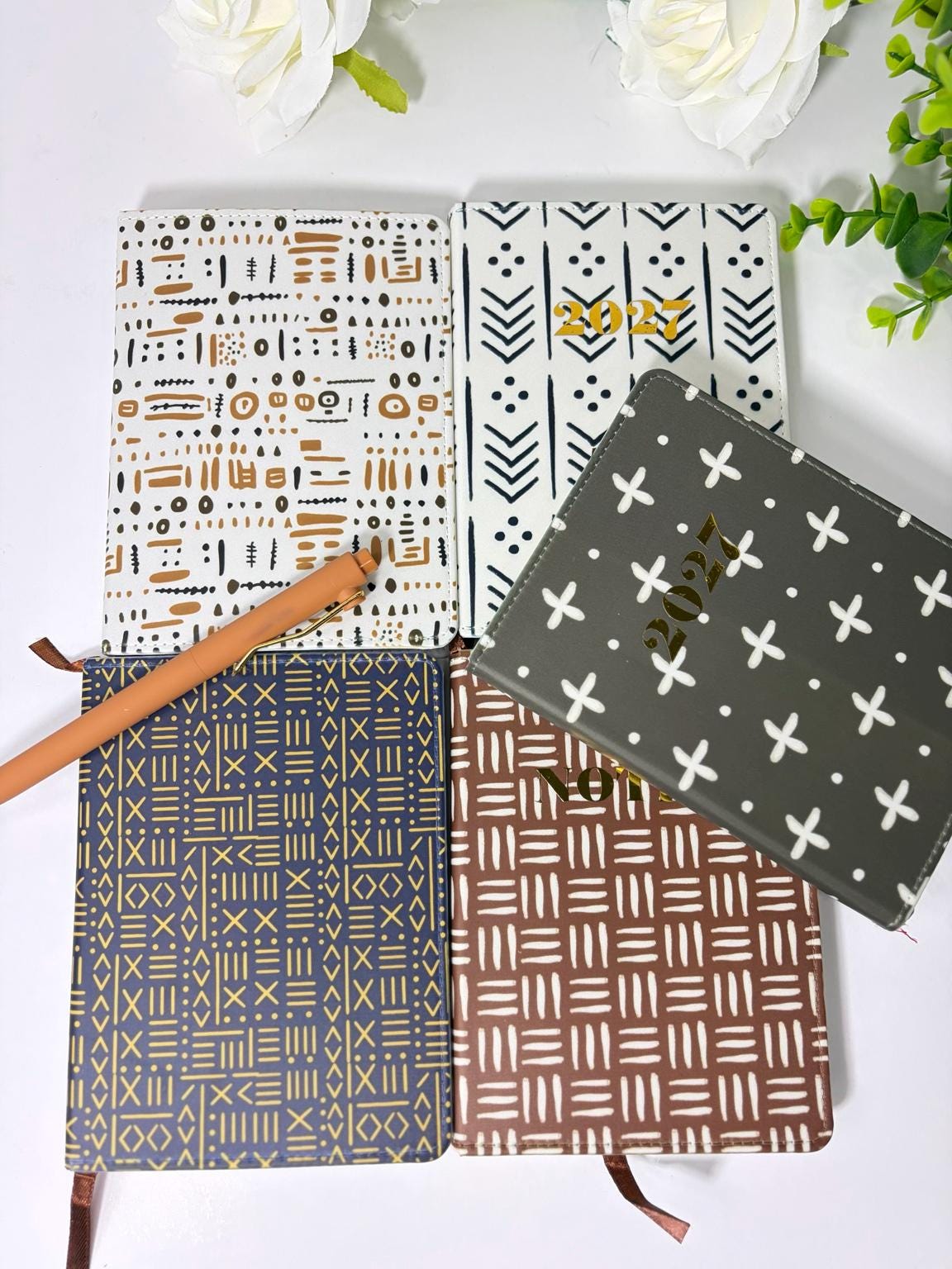 a collection of four patterned notebooks and a pen on a white background.