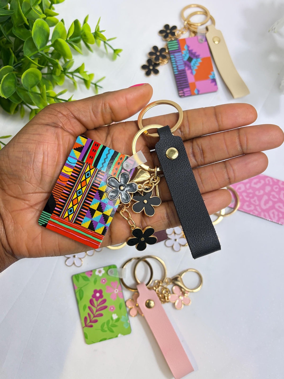 A hand holding a colorful keychain with various charms, including flowers and geometric patterns, against a backdrop of other colorful keychains and accessories.