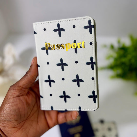 A hand holding a white passport holder with a black and white pattern and the word "Passport" printed on it.