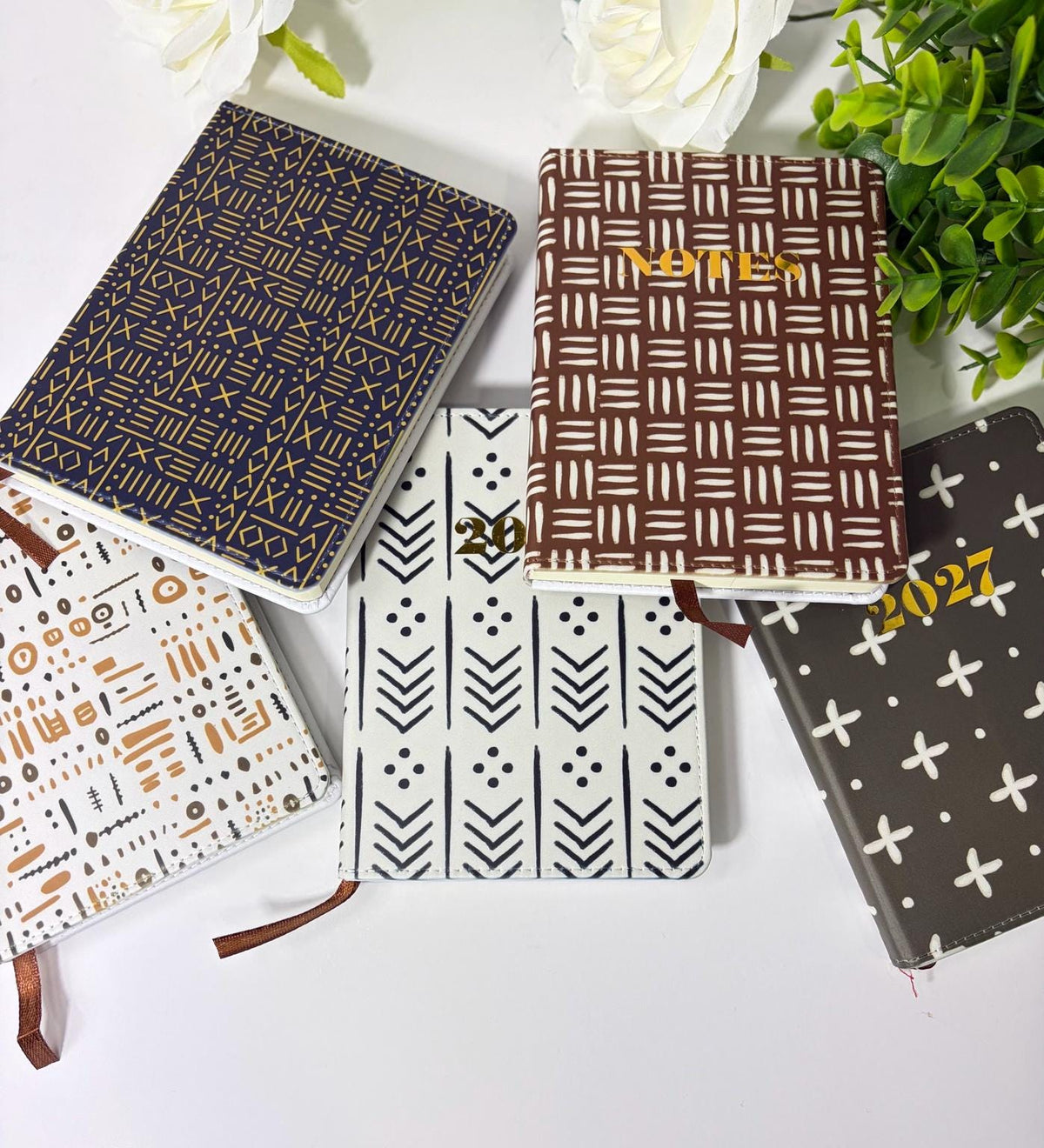 a collection of five different patterned notebooks or planners arranged on a white surface.
