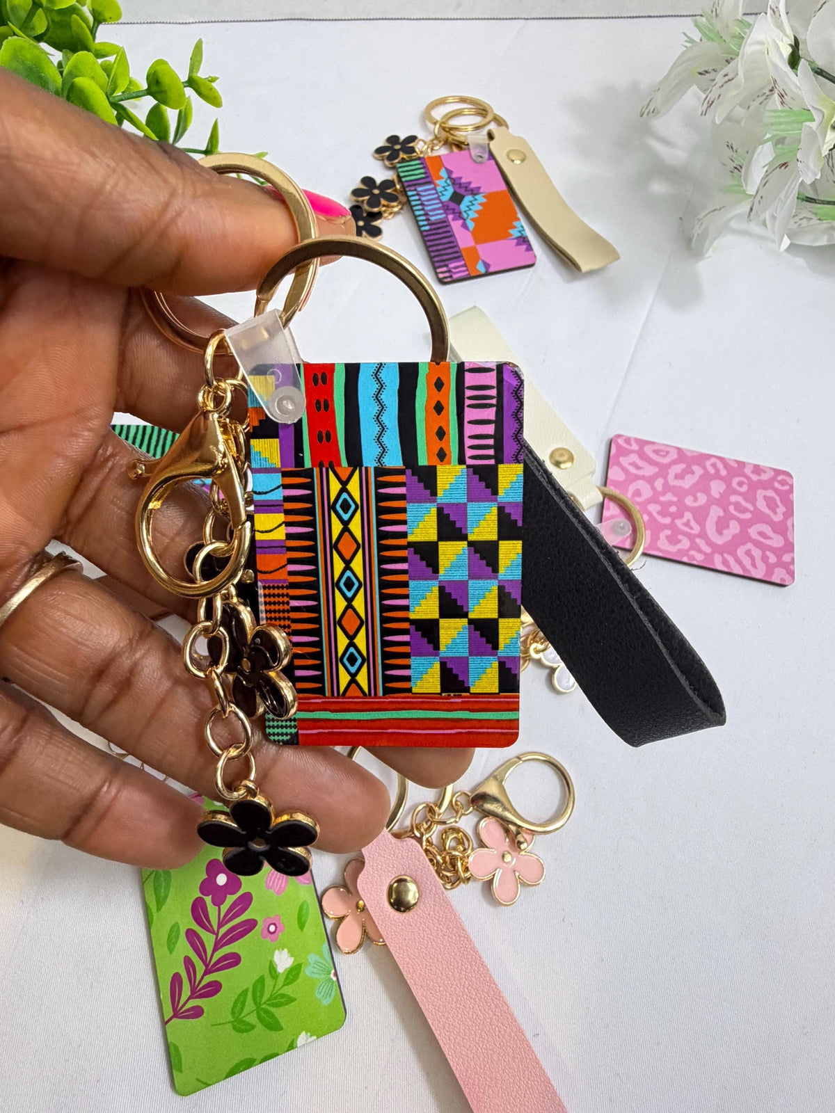 A hand holding a colorful keychain with various patterns and designs, including a floral pattern and geometric shapes.