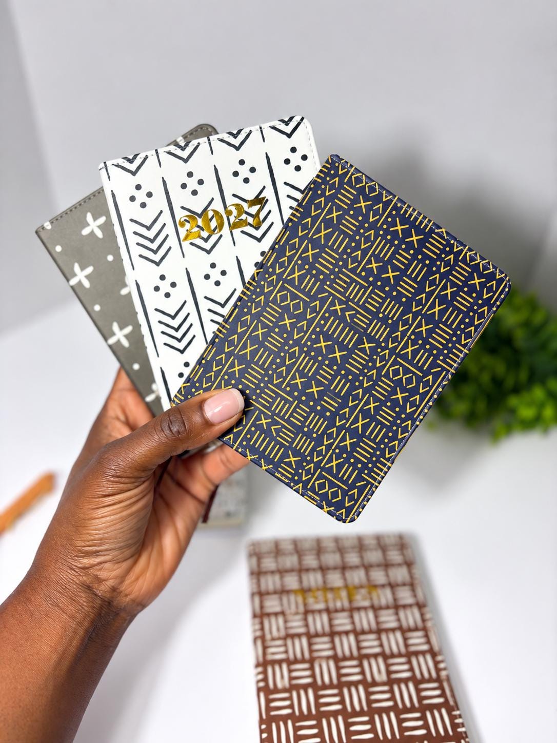 A hand holding three patterned notebooks with different designs.