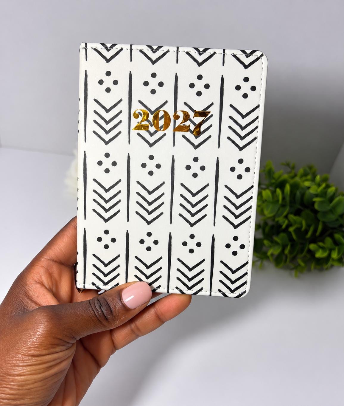A hand holding a white and black patterned notebook with the year "2027" printed on it.