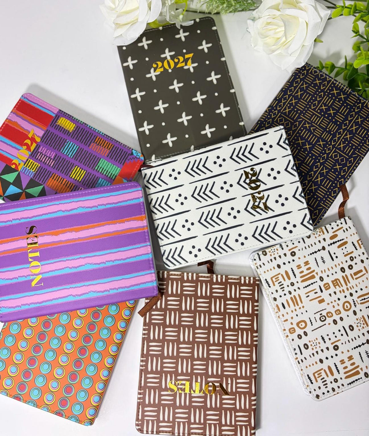 A collection of colorful notebooks and planners arranged on a white surface, with white flowers in the background.