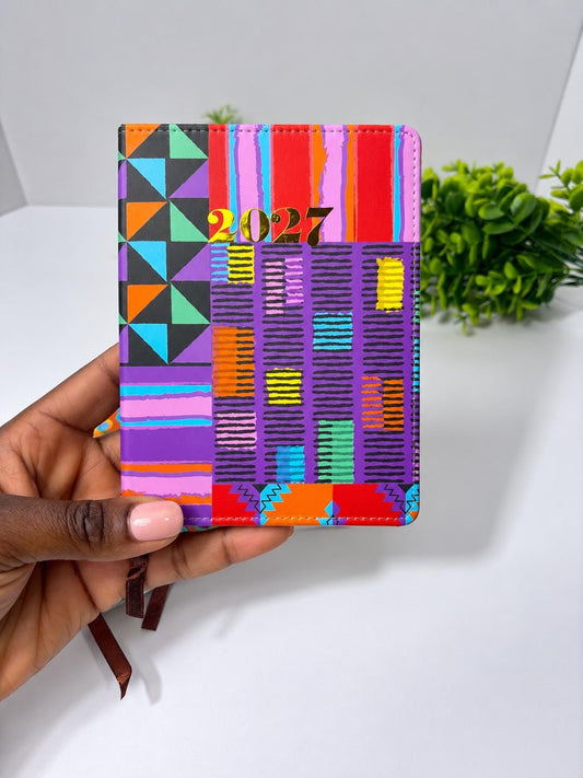 A hand holding a colorful, patterned, and geometric-designed notebook or planner with the year "2027" printed on it.