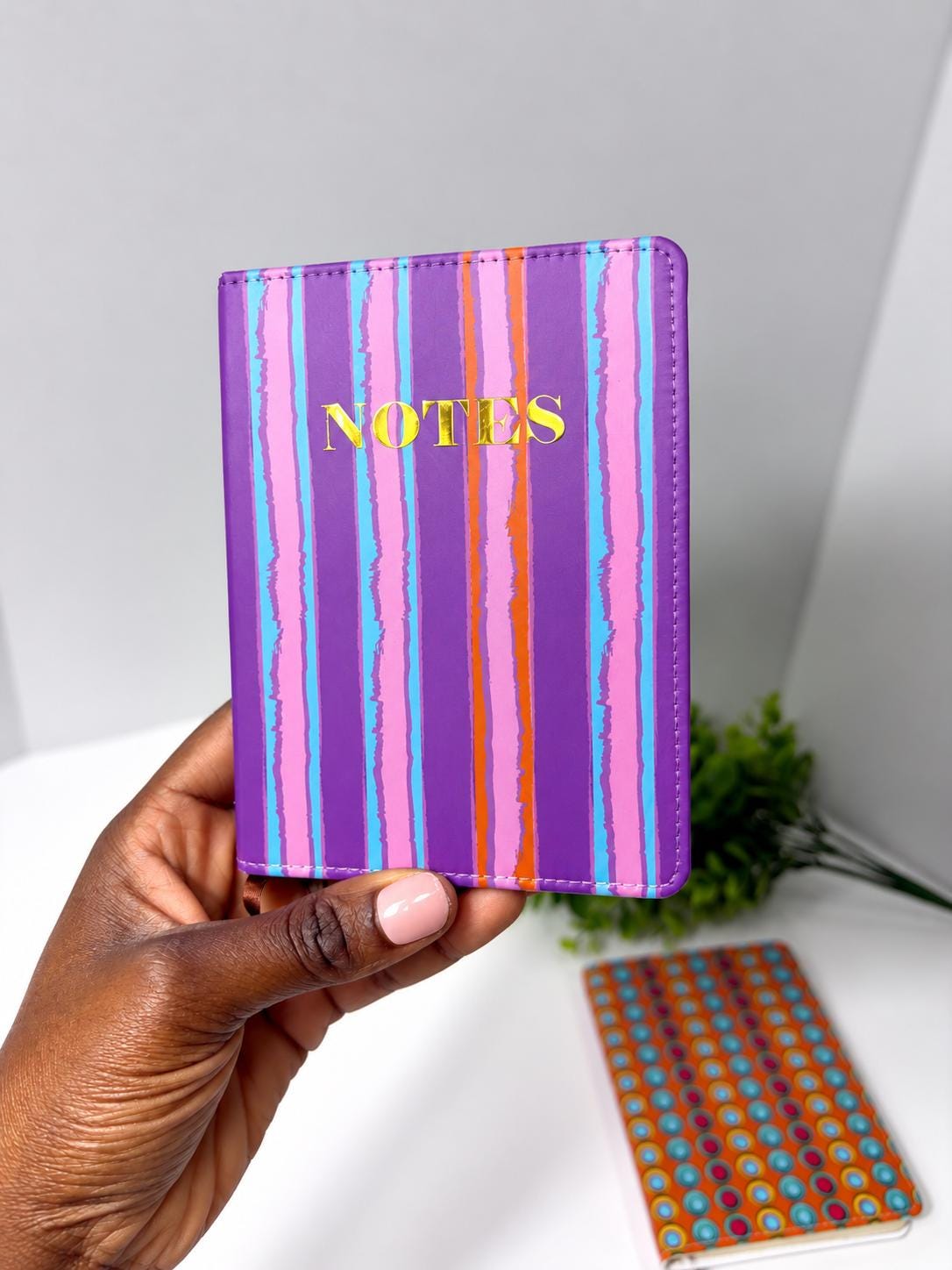 A hand holding a purple notebook with the word "NOTES" printed on it, against a white background.